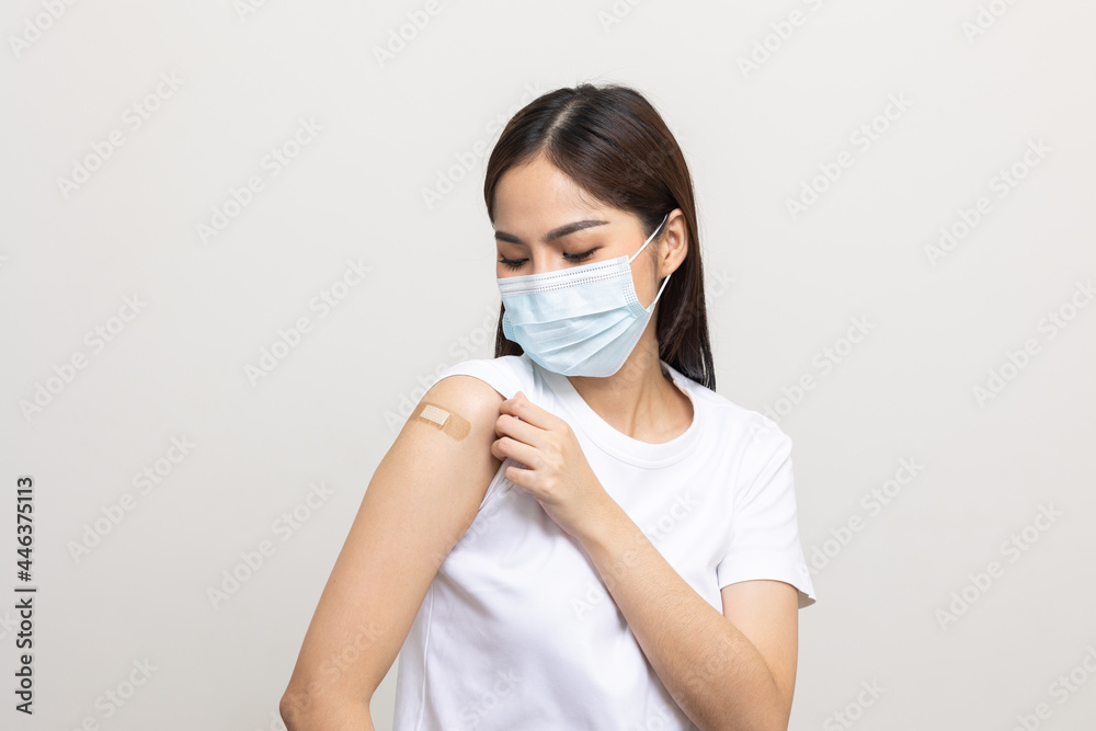 Young beautiful asian woman wearing mask and getting a vaccine protection the coronavirus. Happy female showing arm with bandage after receiving vaccination on isolated white background. Young beautiful asian woman wearing mask and getting a vaccine protection the coronavirus. Happy female showing arm with bandage after receiving vaccination on isolated white background.