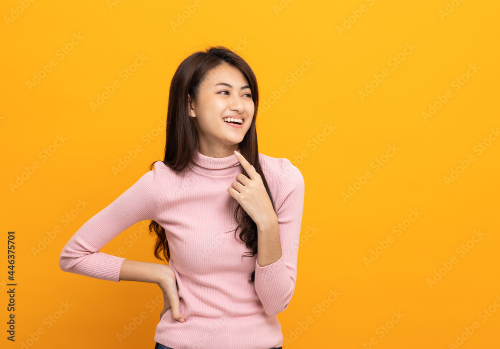 Obraz premium Beautiful asian woman look into blank space. Smiling female wearing pink shirt on isolated yellow background. Attractive Teenager girl looking at empty space for text feeling excited and thinking.