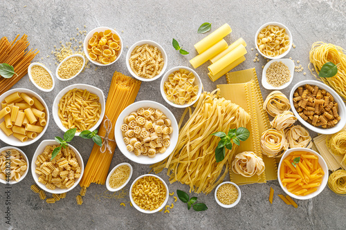 Pasta. Various kinds of uncooked pasta and noodles over stone background, top view with copy space for text. Italian food culinary concept. Collection of different raw pasta on cooking table photo