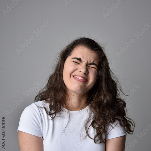 Close up portrait of young woman with natural brown hair, over the top facial expressions on light grey studio background.