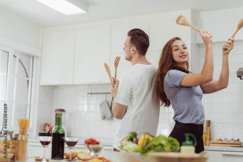 Young Beautiful couple love is dancing while cooking together in the kitchen. Happy loving man and woman cooking healthy food at home.