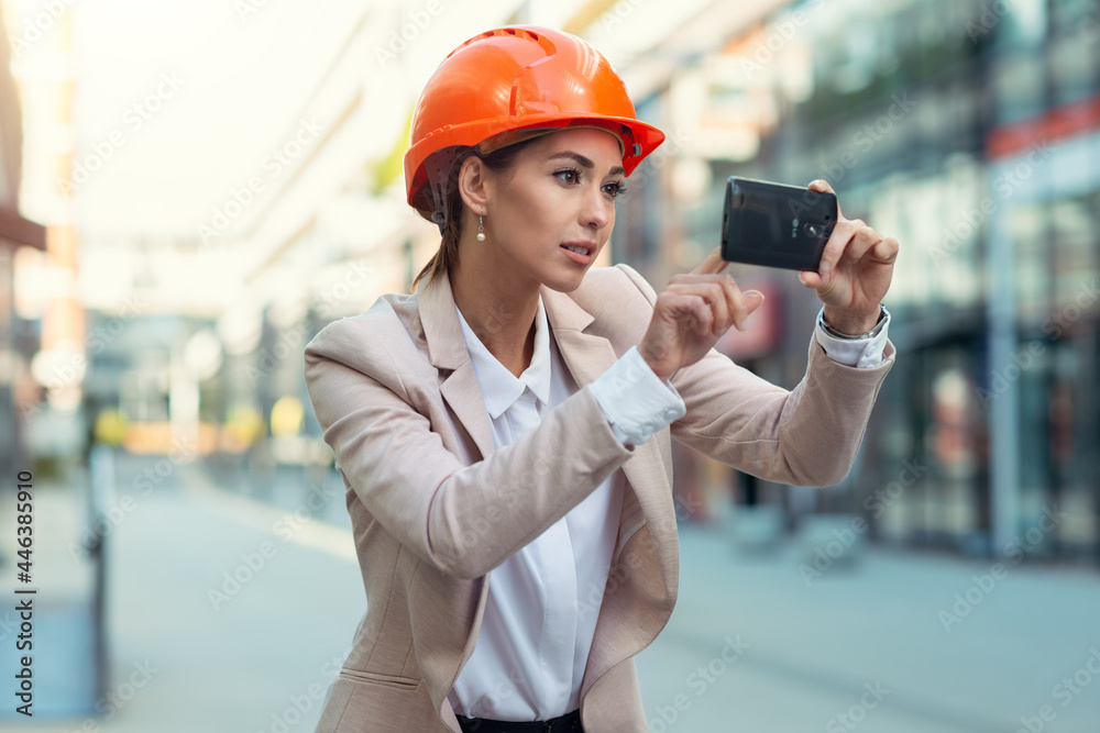 Young beautiful architect girl standing and using phone camera Young beautiful architect girl standing and using phone camera