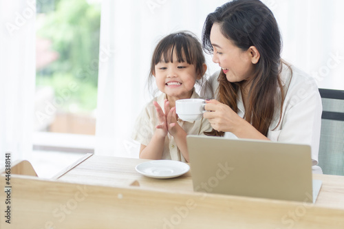 happy parents happy mother holding a cup of coffee happy with daughter While working on a laptop, the computer work in the house on the weekend holiday