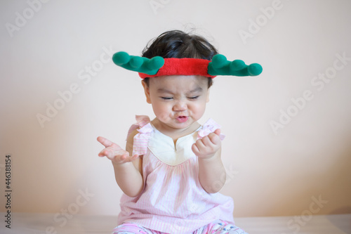 A cute happy little Asian girl who has just had baby teeth do a fun pose. She wears antler hat and look at camera isolated on background. baby expression concept