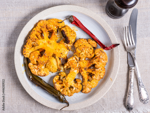 Cauliflower steaks baked with hot pepper on a plate, top view, close-up