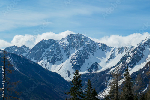 A close up view on the sonw-capped Alps in Slovenia. There are thick, white clouds behind the mountains. There are a few trees in the frame. Idyllic landscape. Cloudy, but sunny day. Calmness © Chris