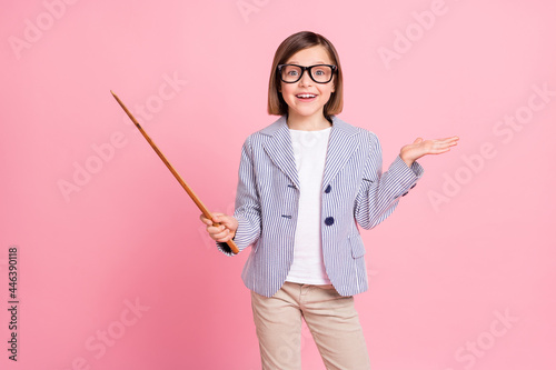 Portrait of attractive cheerful preteen girl showing stick copy space lecture isolated over pink pastel color background