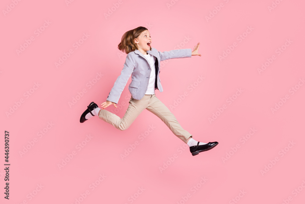 Full length profile photo of astonished small girl jump look empty space wear blazer trousers shoes isolated on pastel pink color background