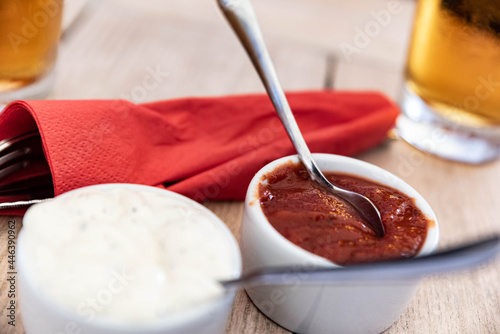 Restaurant table  tomato and garlic pizza sauces with cutlery and a pint of beer on a restaurant table.