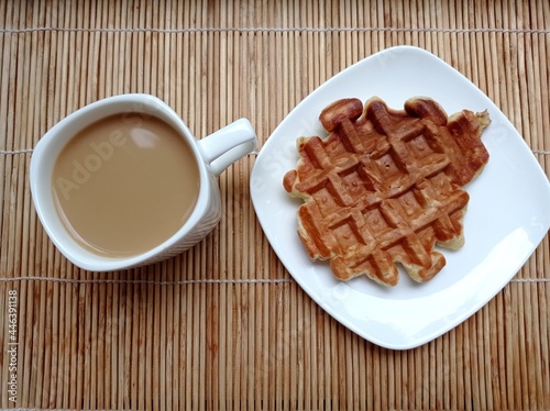 Breakfast. Coffee with milk in a white mug and a waffle on a saucer on a bamboo napkin.