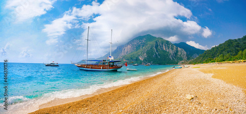 Fototapeta Naklejka Na Ścianę i Meble -  Beautiful panoramic view of sea and beach Cirali, Kemer, Antalya, Turkey. Ship against backdrop of mountains and blue sky with clouds on sunny day.