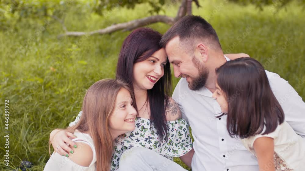 Happy parents spending leisure time with two cute daughters on fresh air. Smiling young family enjoying summer picnic on nature. Concept of people and relaxation. Family enjoying summer picnic Happy parents spending leisure time with two cute daughters on fresh air. Smiling young family enjoying summer picnic on nature. Concept of people and relaxation. Family enjoying summer picnic