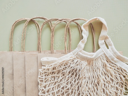Biodegradable paper bags and reusable mesh Cotton shopper on neutral green background. Eco friendly mesh shopper. Zero waste, plastic free concept. Sustainable lifestyle. Top view. Copy space