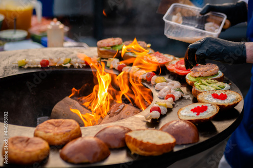 Chef preparing shrimp, prawn skewers and burgers with red caviar, avocado on brazier with hot flame at summer local food market - close up. Outdoor cooking, seafood, gastronomy, street food concept photo