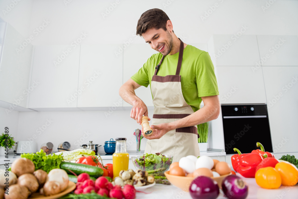 Photo portrait young man in apron cooking vegetables salad adding salt Photo portrait young man in apron cooking vegetables salad adding salt