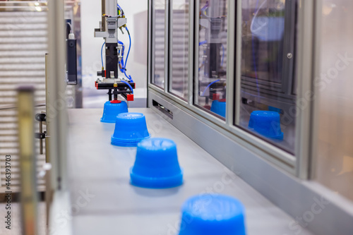 Blue polypropylene pots on conveyor belt of automatic plastic injection molding machine with robotic arm at exhibition, trade show. Manufacturing, industry and automated technology equipment concept