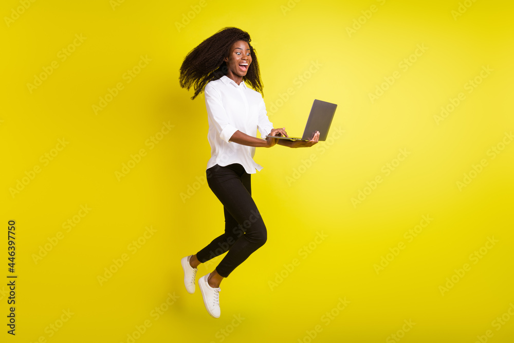 Full length body size photo crazy woman jumping high laughing using computer isolated vivid yellow color background Full length body size photo crazy woman jumping high laughing using computer isolated vivid yellow color background