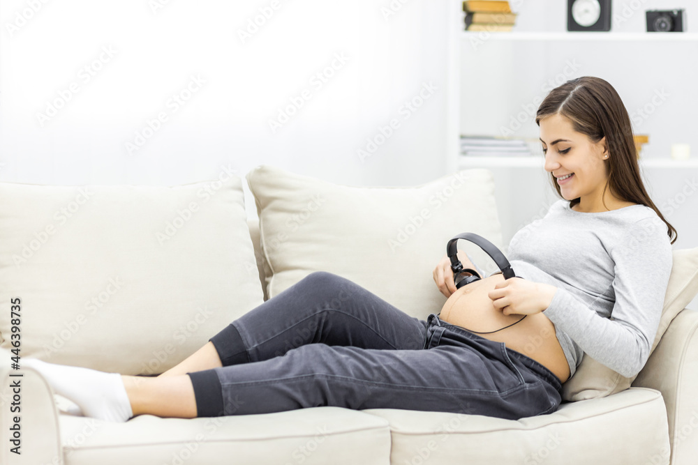 Photo of pregnant woman lying on the sofa with headphones.