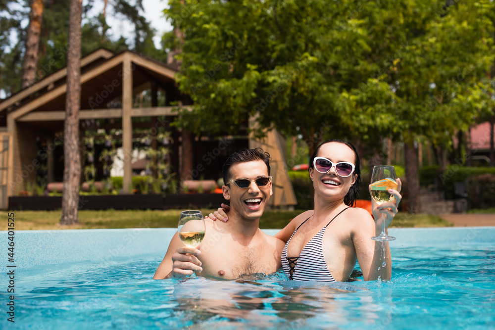 Young couple holding glasses of white wine in swimming pool