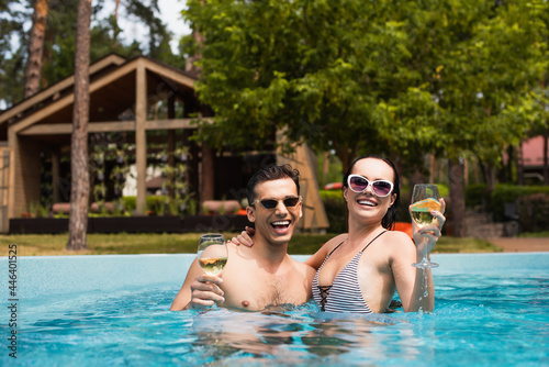 Young couple holding glasses of white wine in swimming pool