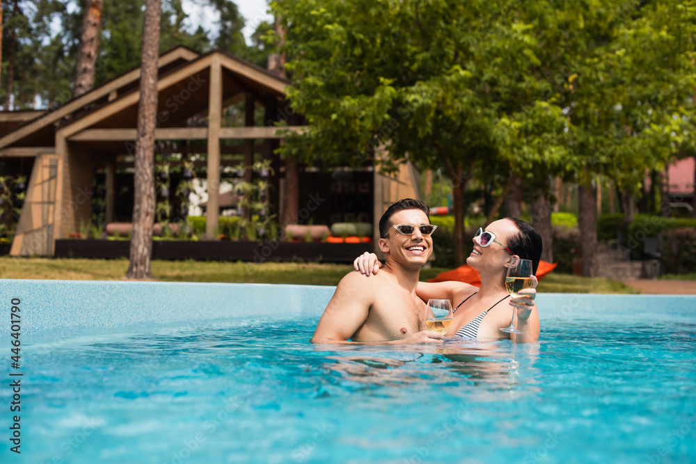 Brunette woman with wine hugging boyfriend in swimming pool on resort