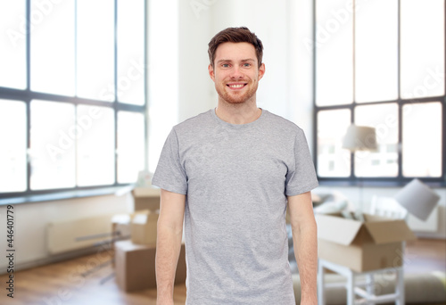 moving, real estate and people concept - happy smiling young man in gray t-shirt and jeans over new home background