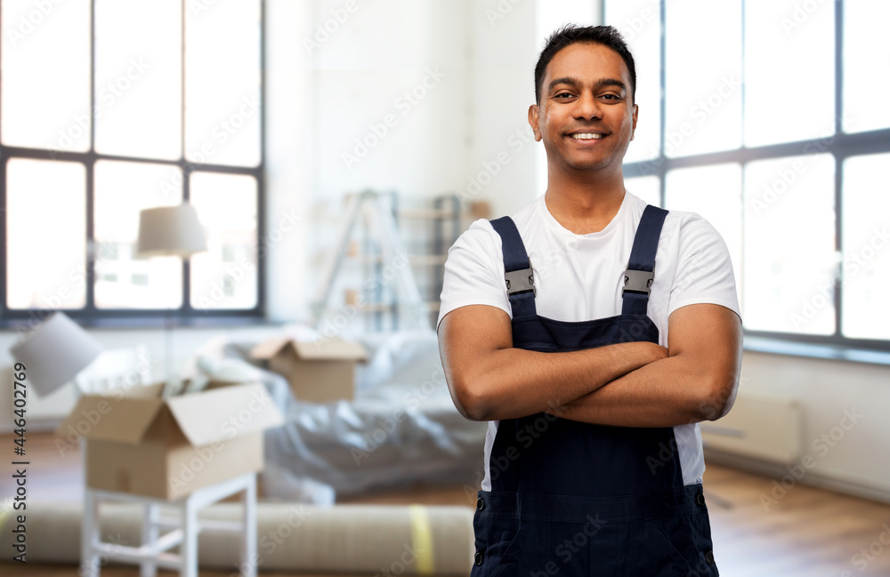 Obraz premium moving, repair and people concept - happy smiling indian worker, loader or repairman with crossed arms over new home background