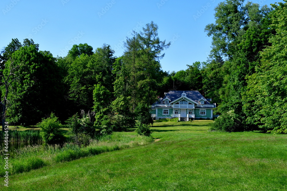 A view of an old abandoned wooden mansion or villa located in the middle of a dense forest or moor next to a well maintained lawn or pastureland seen on a sunny summer day in Poland