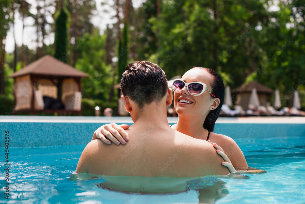 Happy woman in sunglasses embracing boyfriend in swimming pool