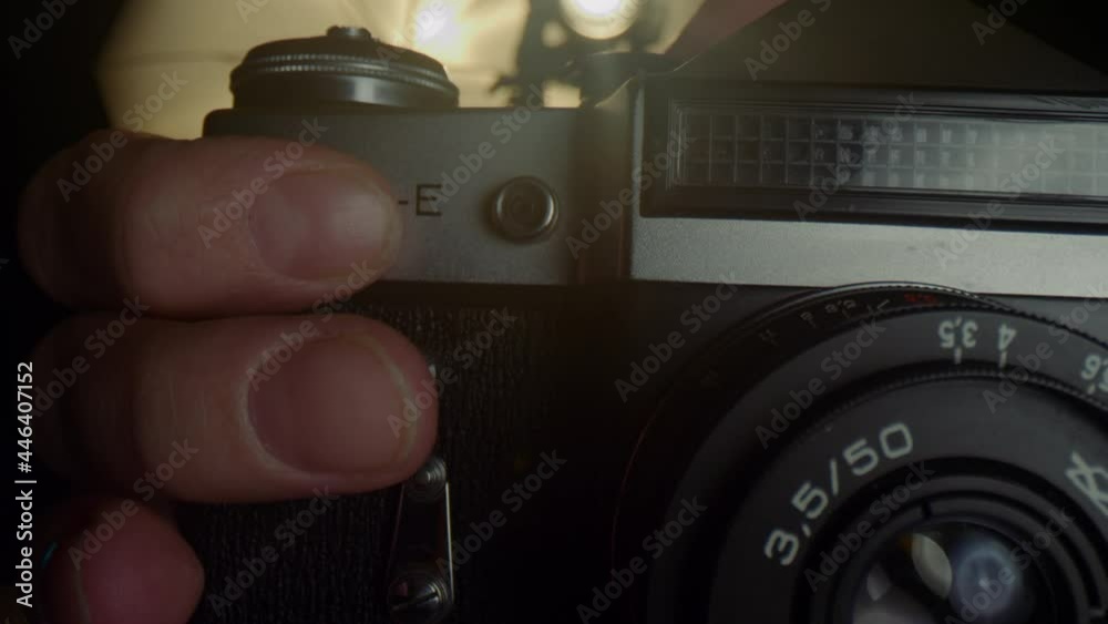 The hands of a male photographer reload a film in an old mechanical camera.