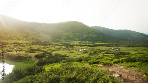 Camping near Lake Nesamovite in the green valley of the Carpathians, landscape overlooking the camp with many tents on sunset.