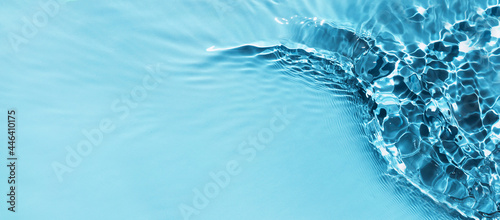 Defocused blue liquid colored clear water surface texture with splashes bubbles with copy space. Water waves in sunlight background. Trendy summer nature banner.  