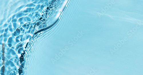 Defocused blue liquid colored clear water surface texture with splashes bubbles with copy space. Water waves in sunlight background. Trendy summer nature banner. 