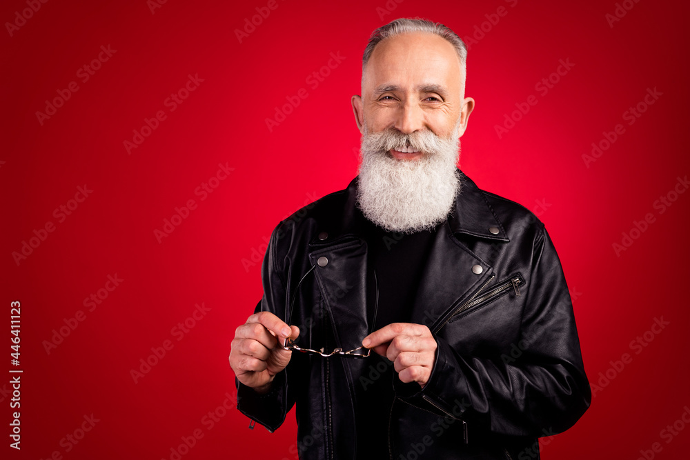 Portrait of attractive cheerful fashionable grey-haired man holding in hand specs isolated over bright red color background Portrait of attractive cheerful fashionable grey-haired man holding in hand specs isolated over bright red color background