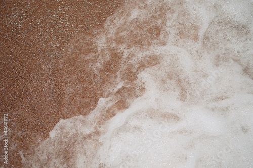 Ocean foamy wave on the sandy beach background 