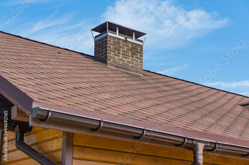Foto Bitumen asphalt roofing shingles and brick chimney pipe on a wooden house