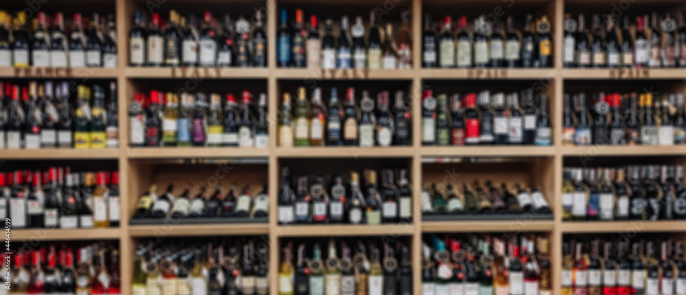 Blurred image of Various wine bottles sale on the wooden shelf in a supermarket shop.