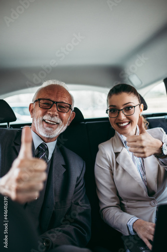 Good looking senior business man and his young woman colleague or coworker sitting on backseat in luxury car. Transportation in corporate business concept. photo