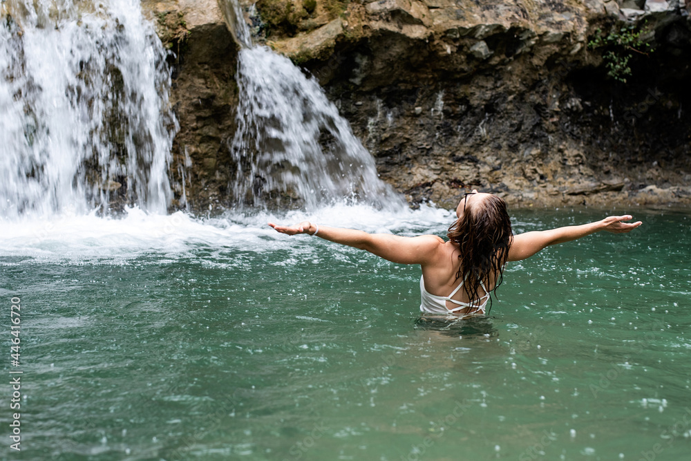 Woman swimming in the mountain river with a waterfall Woman swimming in the mountain river with a waterfall