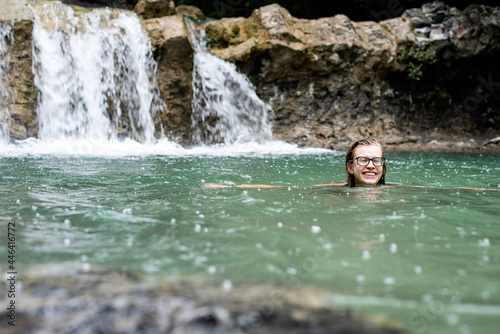 Woman swimming in the mountain river with a waterfall