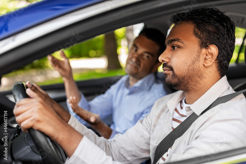 driver courses and people concept - driving school instructor talking to sad indian man failed exam in car