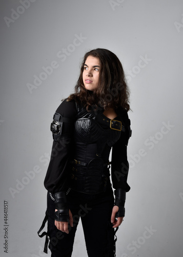 Close up portrait of young woman with natural brown hair   wearing black leather scifi outfit with corset  standing pose on light grey studio background.