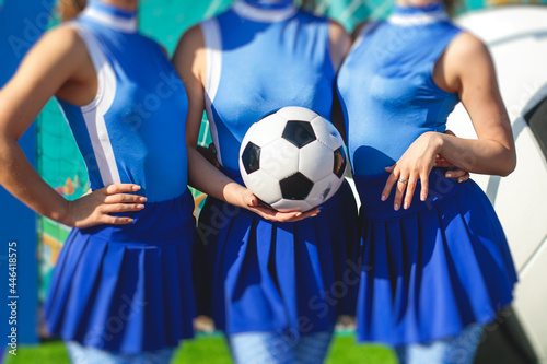 Female group of cheerleader in action, wearing white blue uniform with audience in the background performing and supporting during football game match © tsuguliev