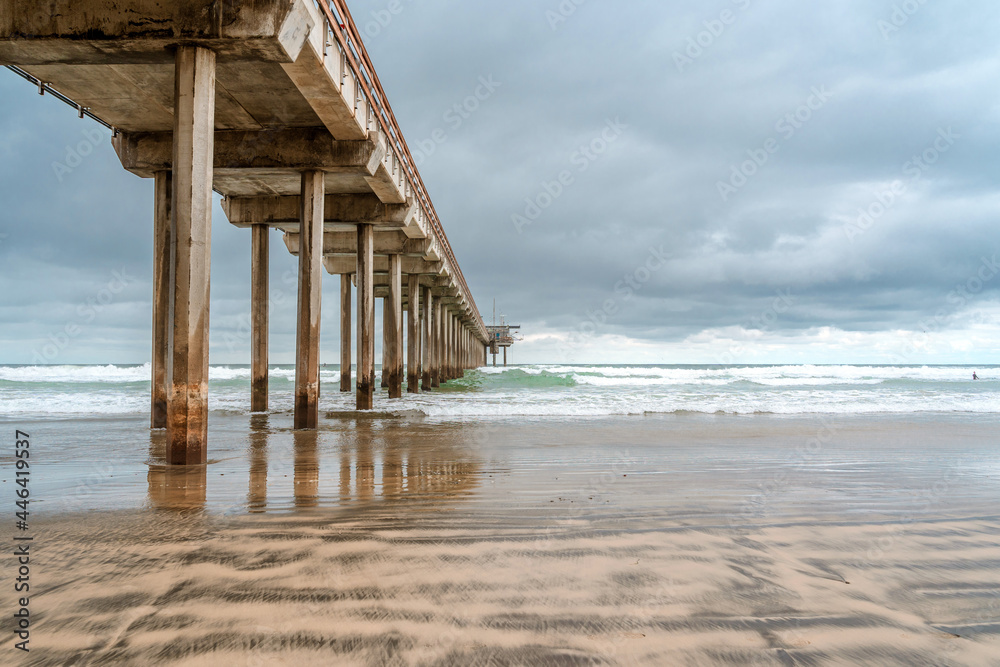 A dramatic landscape on the ocean in cloudy weather, a beautiful pier in in La Jolla California. Striped sand on the beach