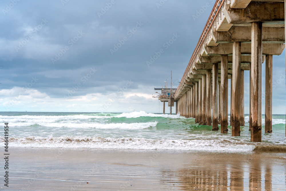 A dramatic landscape on the ocean in cloudy weather, a beautiful pier in in La Jolla California. Striped sand on the beach