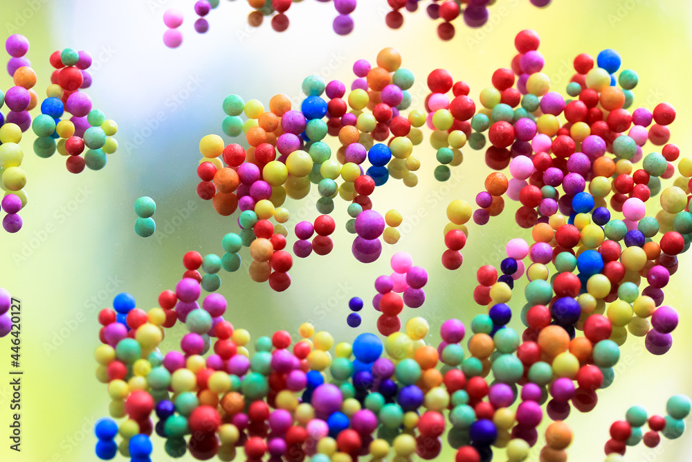 Foam polystyrene round bright colorful beads are reflected on a surface of a glass, mirror. Multicolored pearls floating down, hanging in the air. Foam spherical background. Celebration, fun concept.