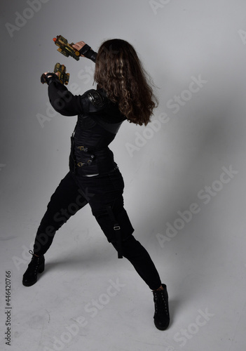 Full length portrait of young woman with natural brown hair,  wearing black leather scifi outfit with corset, standing pose on light grey studio background. © faestock