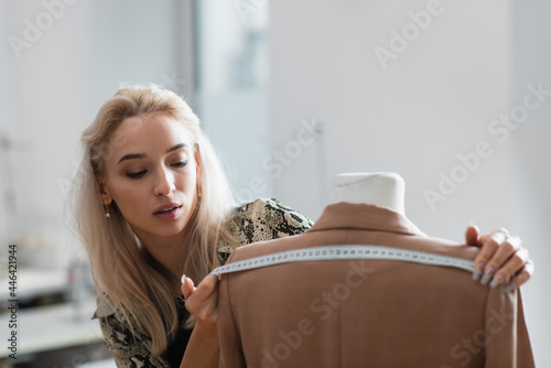 young fashion designer measuring blazer on mannequin in fashion workshop photo