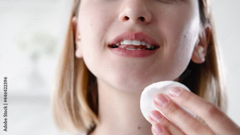 Skin care. Facial cleansing. Freshness hygiene. Morning routine. Unrecognizable relaxed smiling woman with radiant flawless face applying tonic using cotton pad on light. Skin care. Facial cleansing. Freshness hygiene. Morning routine. Unrecognizable relaxed smiling woman with radiant flawless face applying tonic using cotton pad on light.