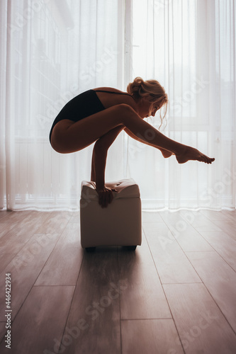 A beautiful girl in a sports swimsuit is doing yoga, practicing different asanas on a cube